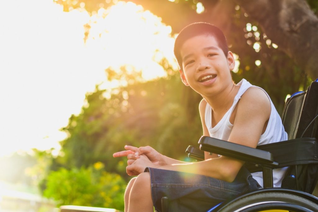 Disabled Asian boy in wheelchair smiling at the camera